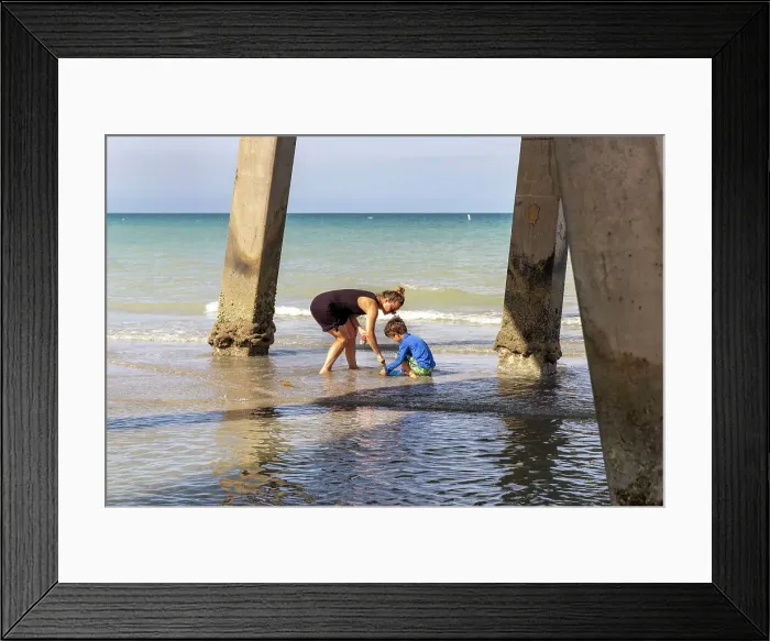 Framed Print : Mother and child playing at the beach, under a pier Framed Print : Mother and child playing at the beach, under a pier