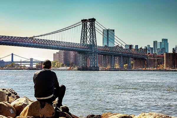 New York City, NY, Williamsburg Bridge with skyline from Grand Ferry Park, man on rock
