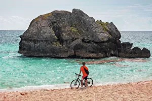 Island Prints: Bermuda, Warwick Long Bay, cyclist standing on beach with aquamarine water and pink sand